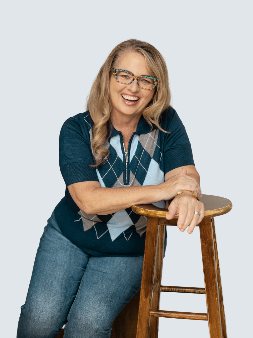 Betsy Kimmel, ICF coach and E-RYT 500 yoga teacher, smiling while seated on a wooden stool